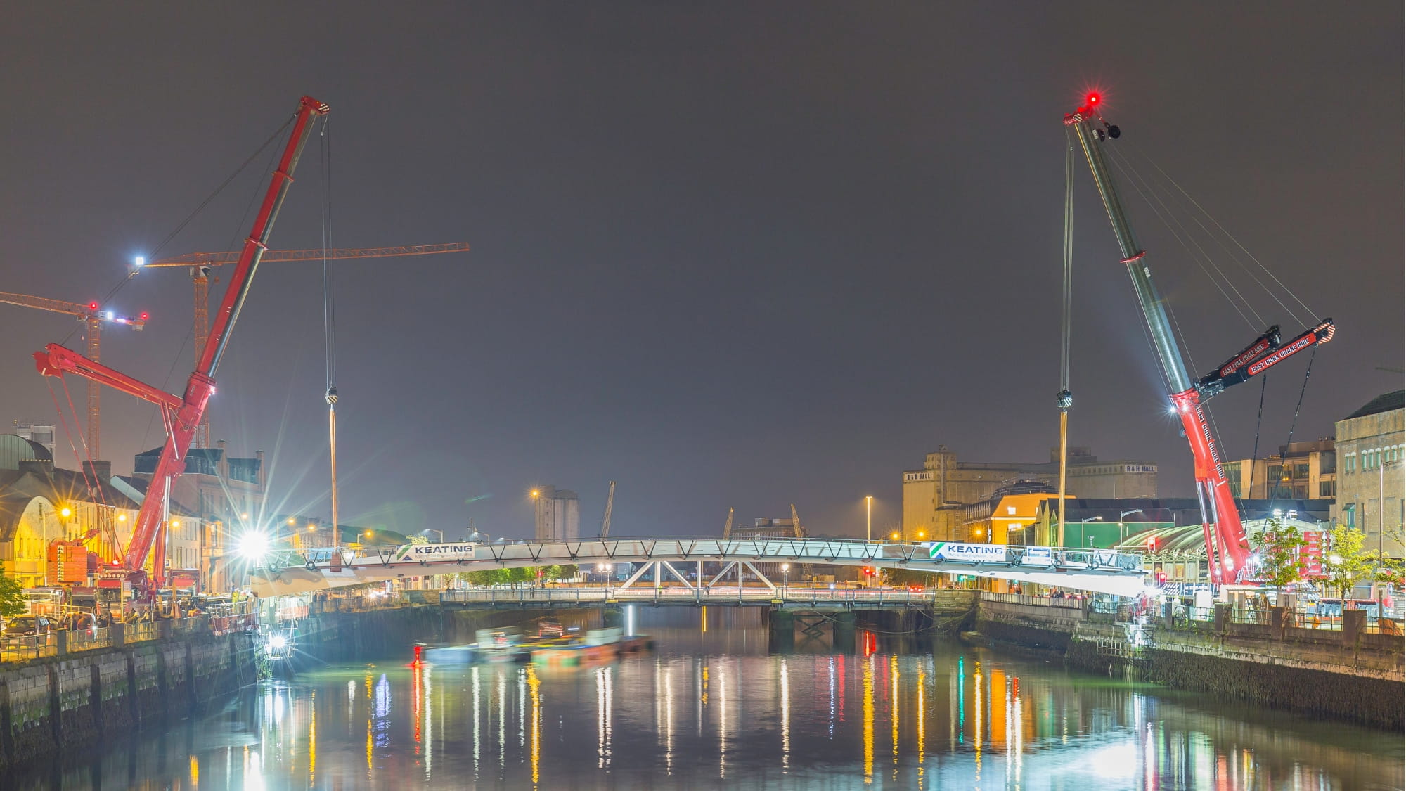 Mary Elmes Bridge being lifted into position at night by two cranes.