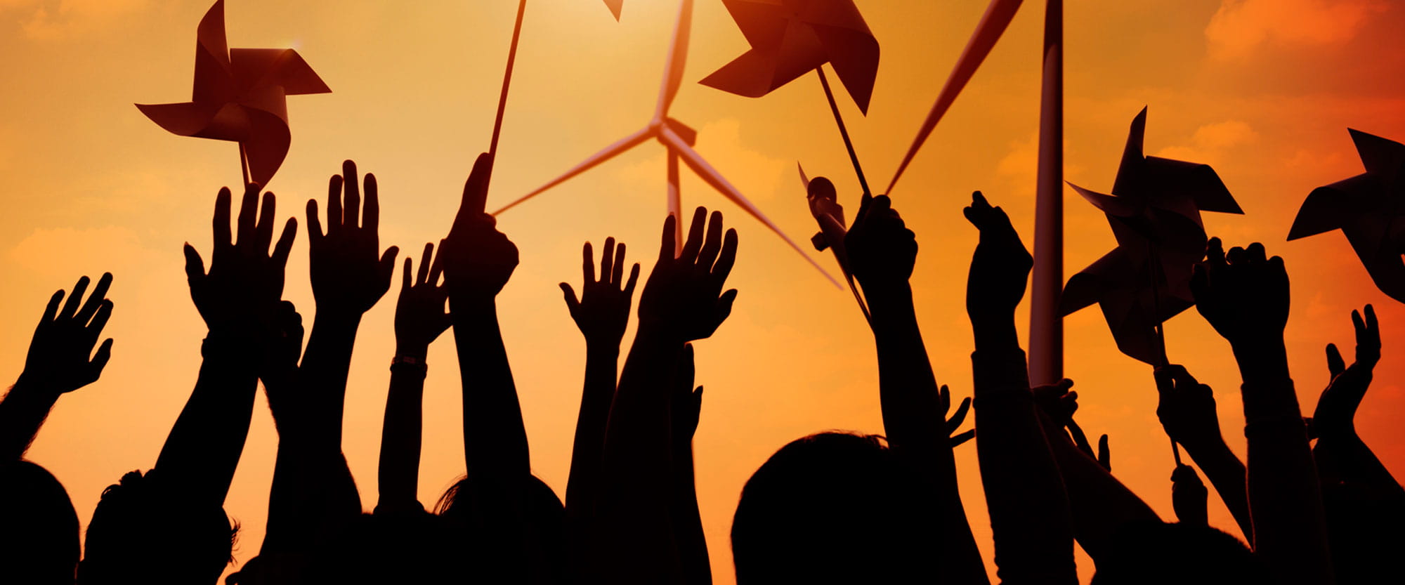 Group of people holding pinwheels with wind turbines in the background
