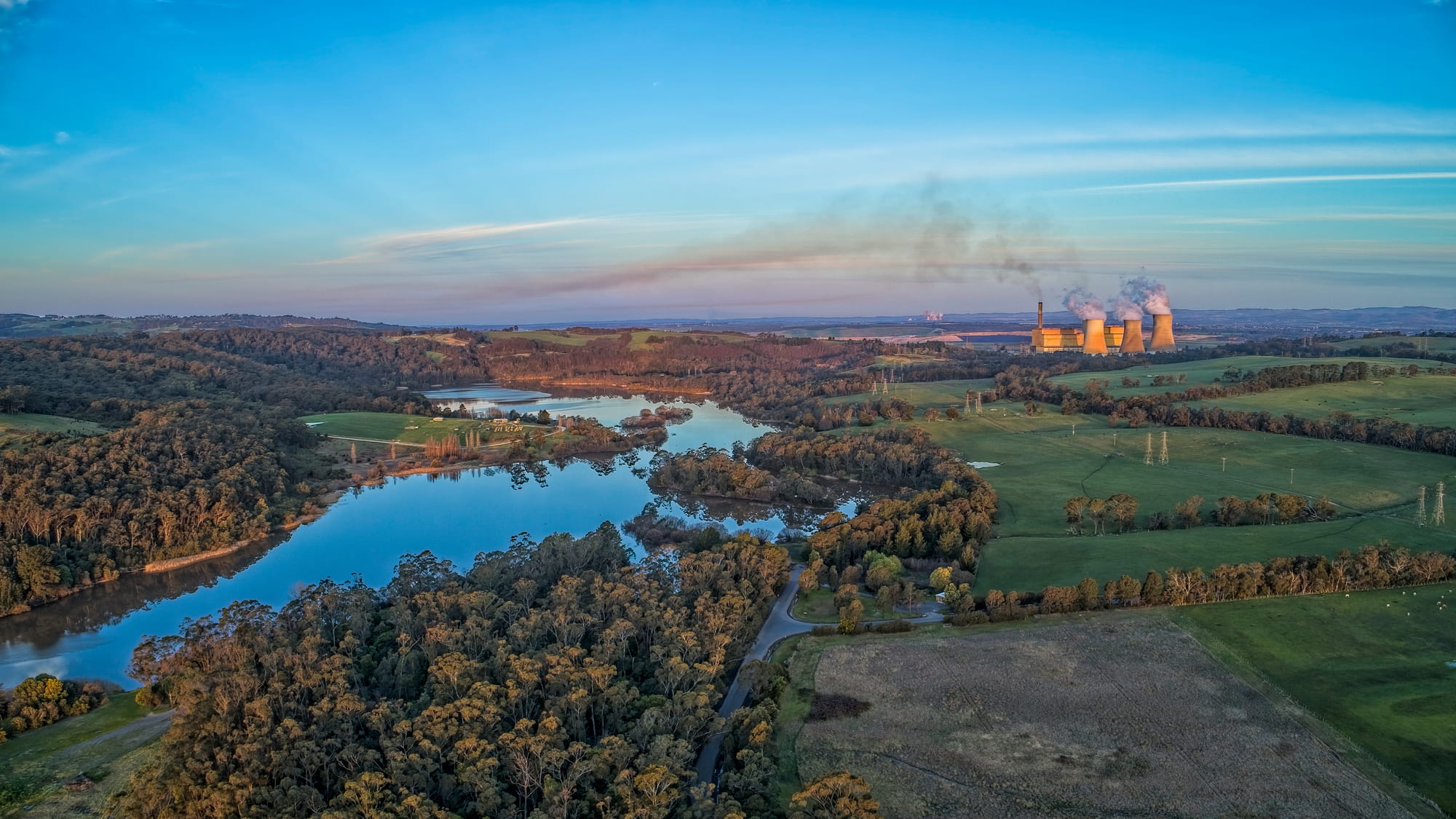 Aerial view over lands and river in country Australia. In the back ground is a power station plant with fumes expolling from the stacks. 