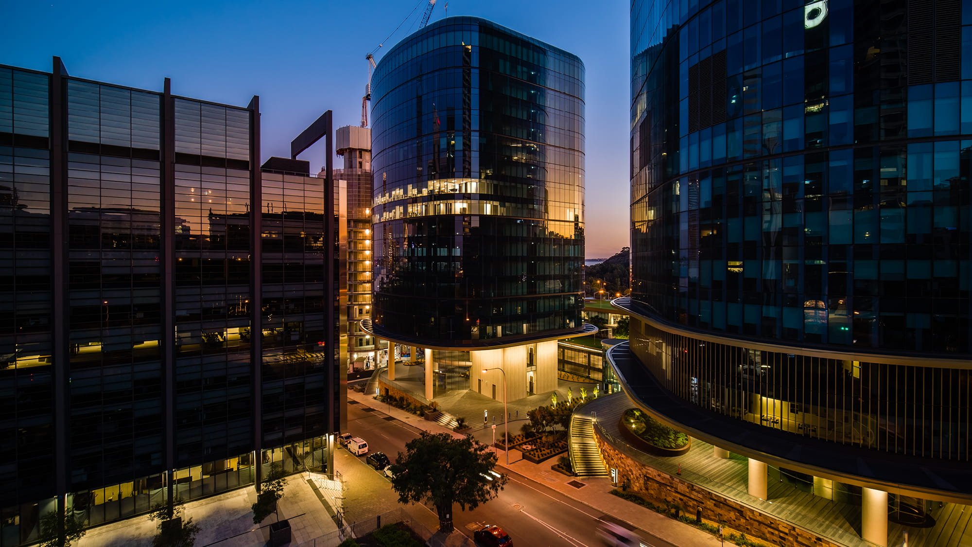 Photograph at night of an office tower in between a carpark tower and another taller office tower