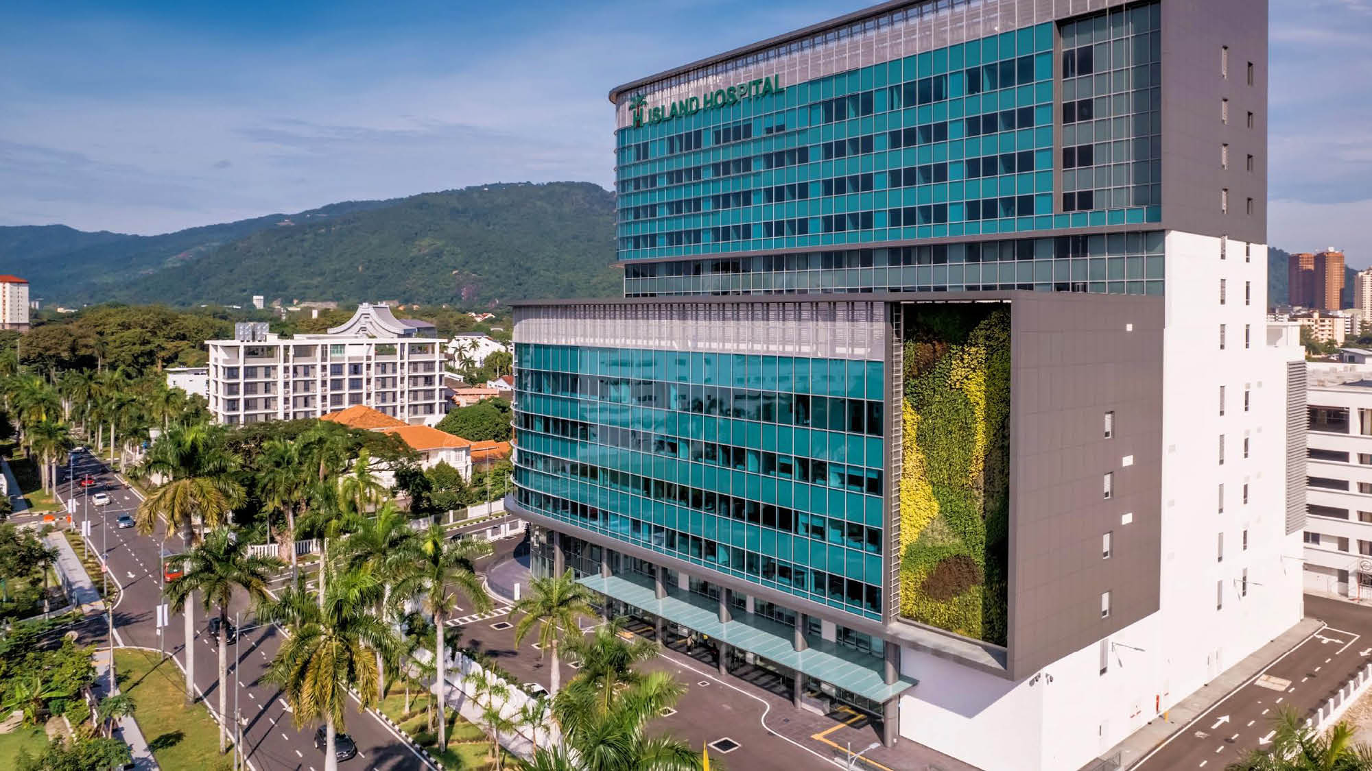 View of  the Island Hospital in Penang city at day time. It's a mulitstorey building with blue panelling on the facade and a street level carpark.
