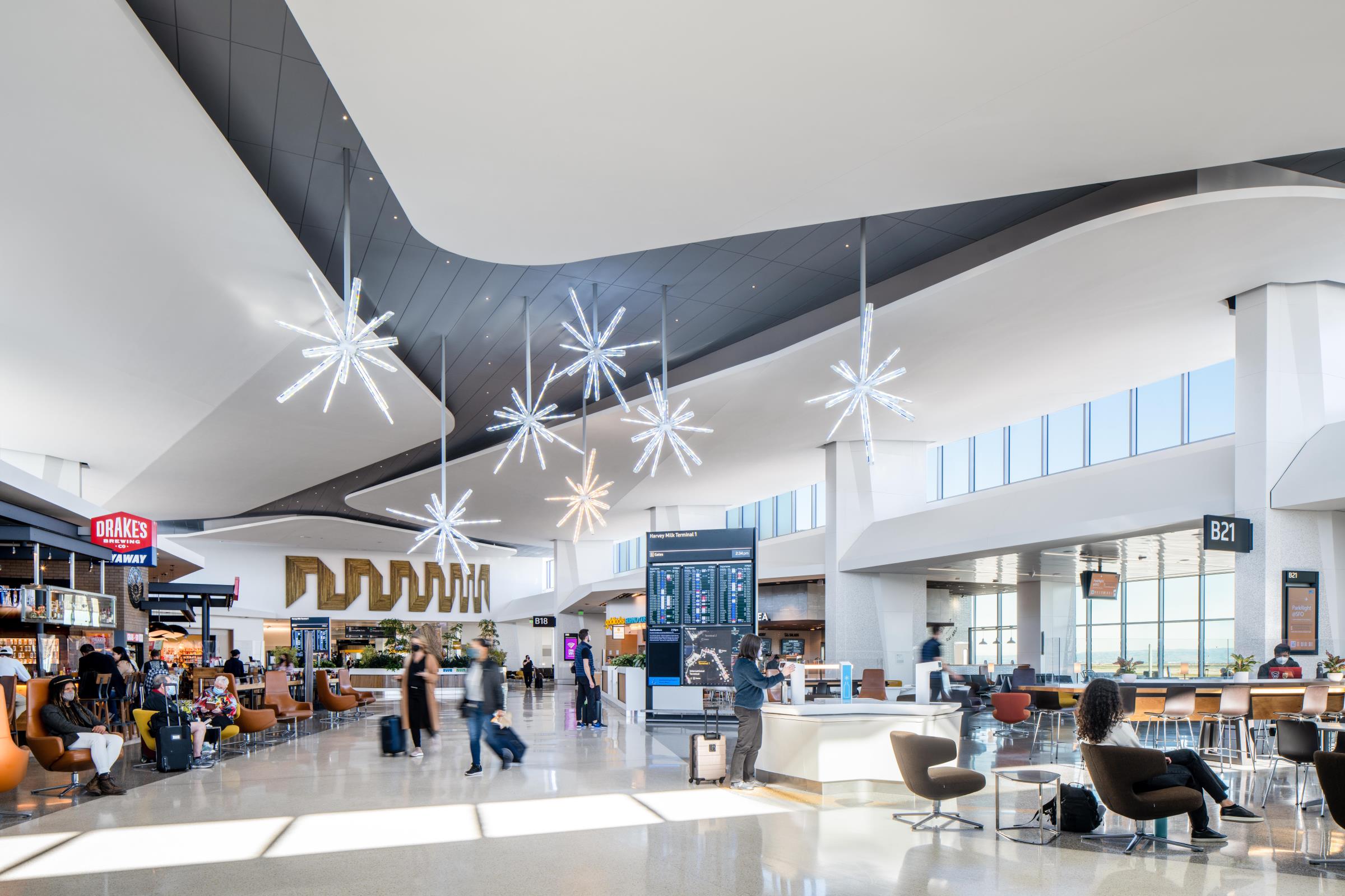 Airport travelers walking through a bright, sunlit airport terminal.
