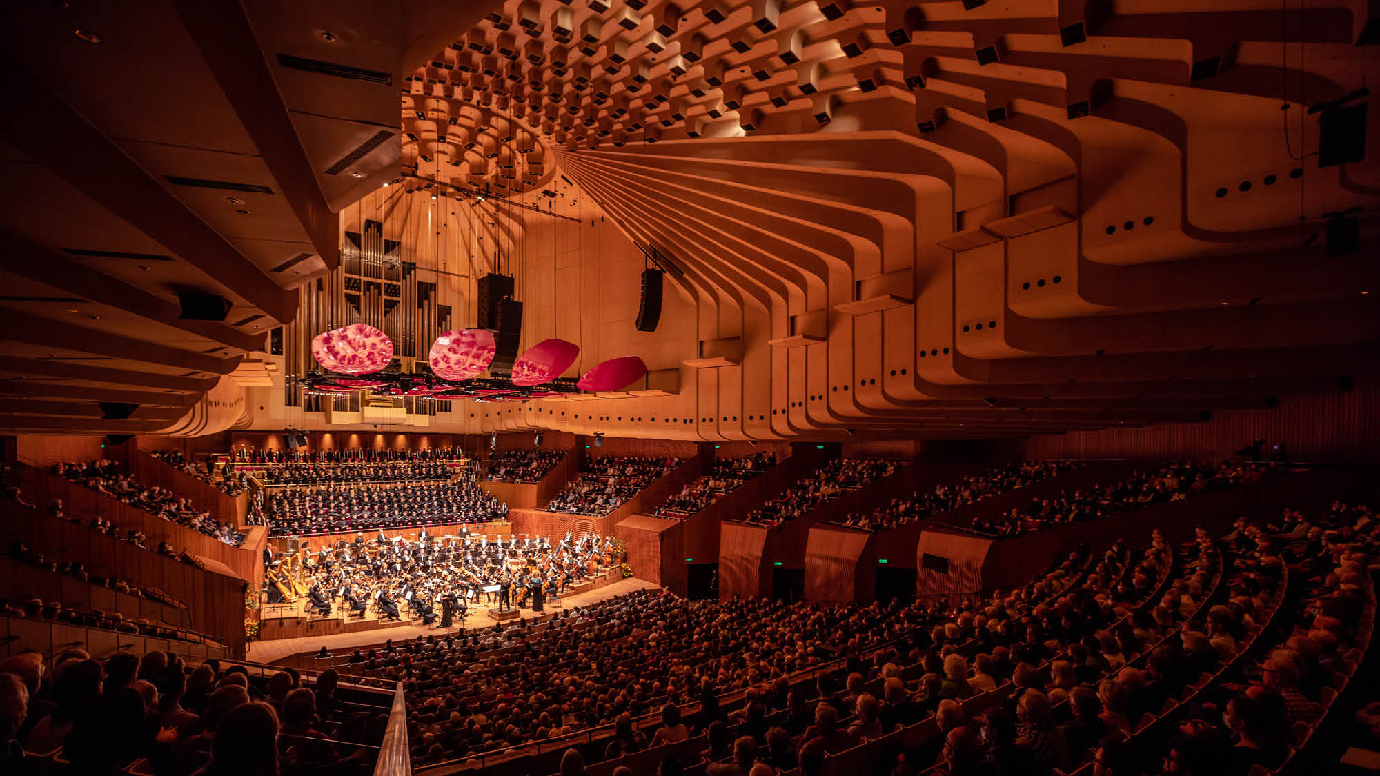 A large concert hall with tiers of seating, dimmed lights and an orchestra on stage