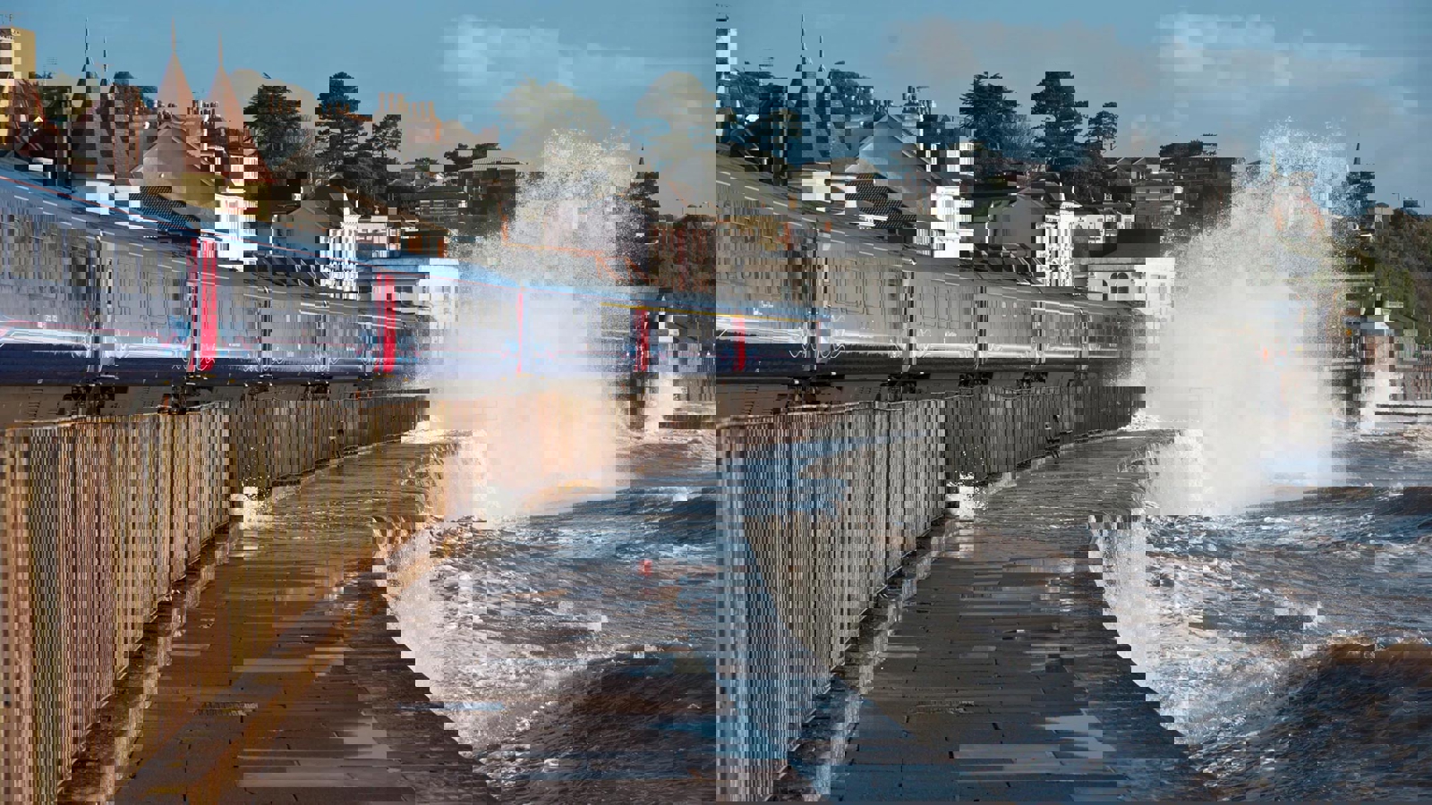 Train running along the coastline with waves throwing up water close to the track