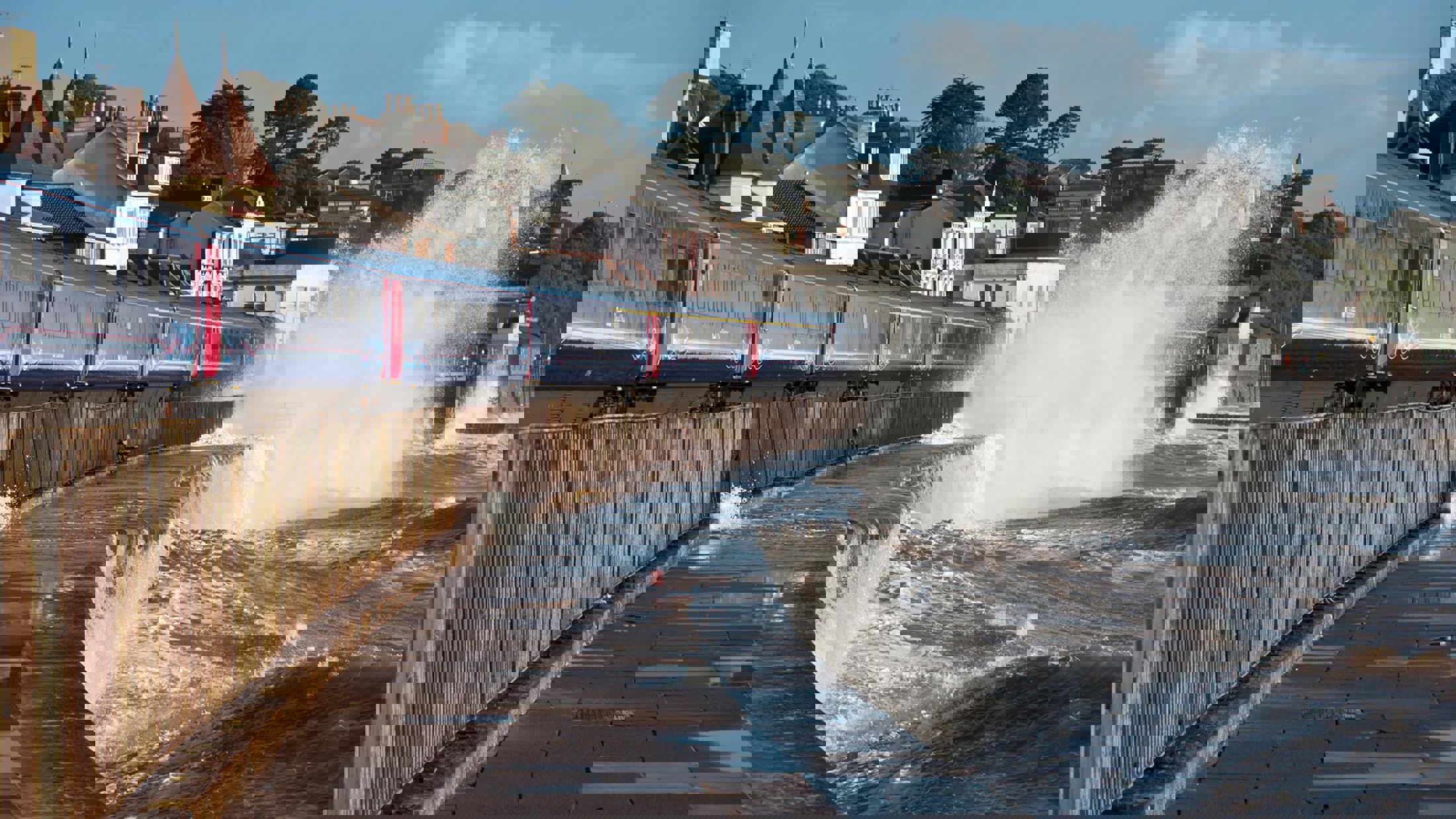 Train running along the coastline with waves throwing up water close to the track