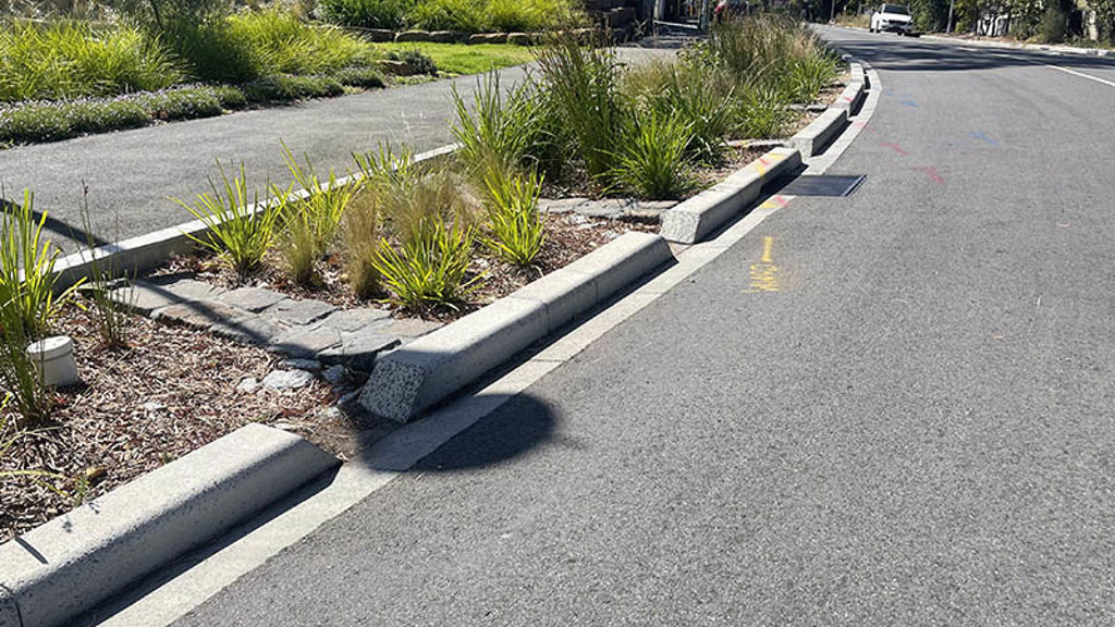 Extended curb alongside road with garden bed with pavers, pebbles and plants
